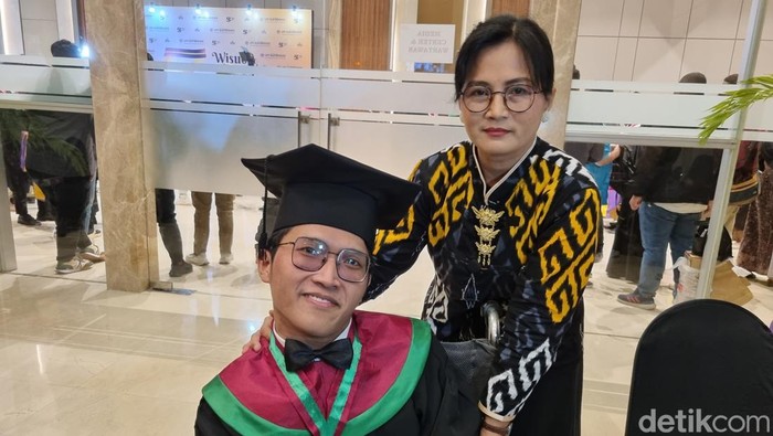 David mahasiswa nonis difabel lulus cumlaude di UM Surabaya bersama orang tua. (Foto: Esti Widiyana/detikJatim)
